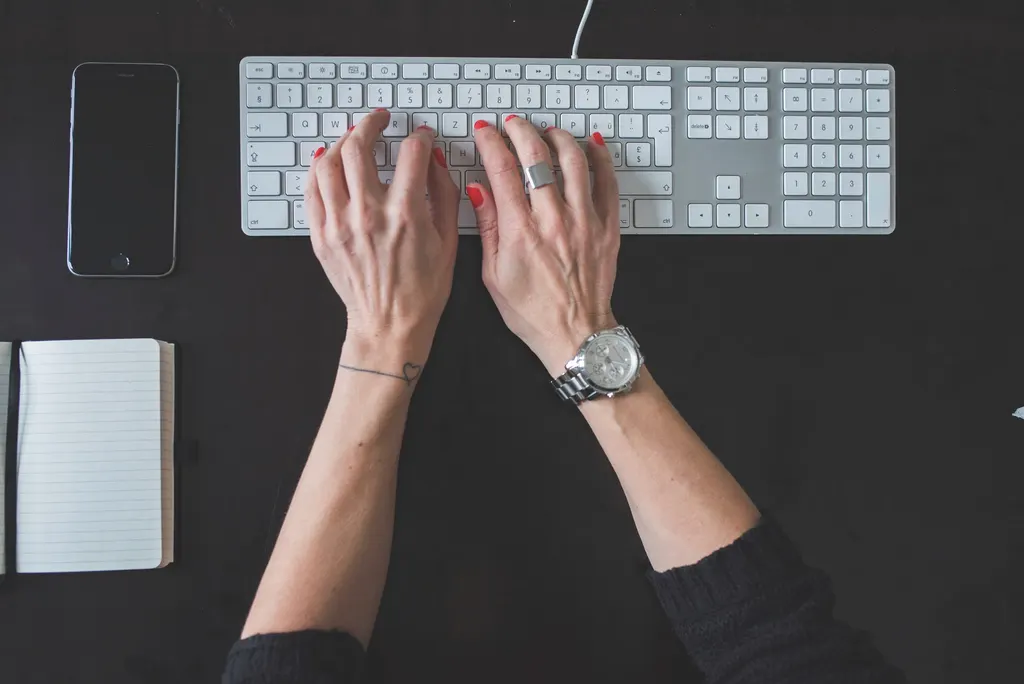 Hands typing on a white computer keyboard on a dark desk